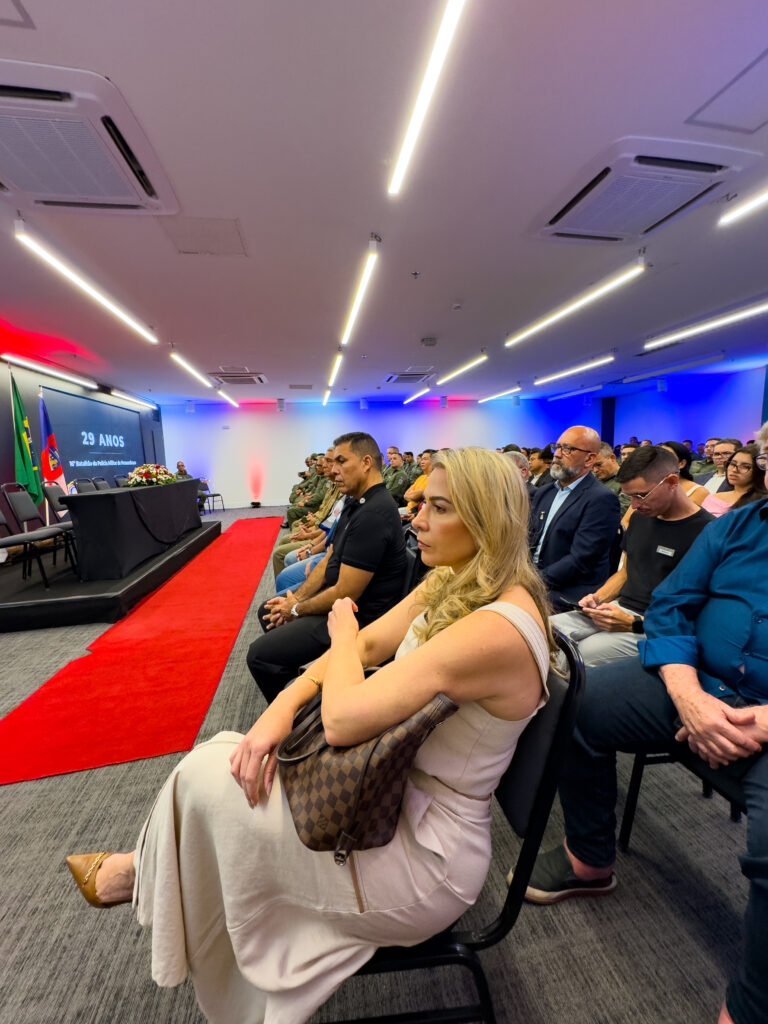 Dir. Tatiana Menezes assistindo a solenidade de homenagem da Polícia Militar.